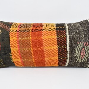 Op de afbeelding: Een lang rechthoekig kussen met een patchwork-ontwerp. Het kussen is gemaakt van geweven stof in tinten oranje, bruin en zwart. De stof heeft een geometrisch patroon.