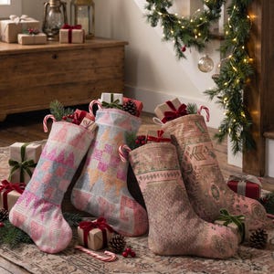 Peut inclure: Quatre chaussettes de Noël présentant des motifs tissés variés dans des tons sourds de rose, d'orange et de marron. Chaque chaussette est remplie de petits cadeaux emballés et de sucres d'orge, avec des motifs géométriques complexes.