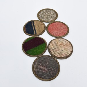 May include: Six round fabric coasters with a brown trim. The coasters have different patterns, including a red, a green and a blue pattern.
