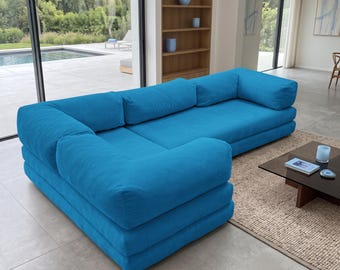 Può includere: Un divano angolare a forma di L di colore blu brillante in tessuto di velluto a coste testurizzato. Il divano presenta un design a profilo basso con sedute spesse e imbottite, braccioli larghi e una struttura modulare.