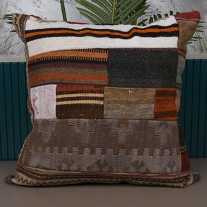 May include: Square patchwork pillow with a variety of colors and textures. The pillow features a mix of brown, orange, white, and gray patches. The design includes stripes and geometric patterns, creating a rustic, handcrafted look. A decorative accent for a sofa or bed.