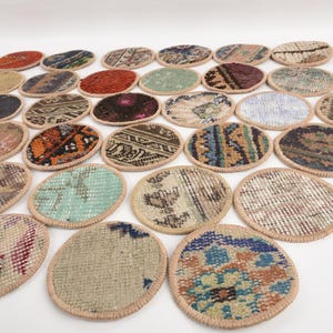 May include: A collection of oval-shaped coasters with a woven rug design. The coasters feature various colors, including red, blue, green, and brown, with a beige border. The coasters are arranged on a white surface.