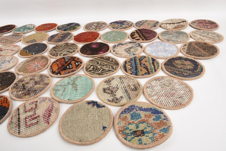 May include: A collection of oval-shaped coasters with a woven rug design. The coasters feature various colors, including red, blue, green, and brown, with a beige border. The coasters are arranged on a white surface.