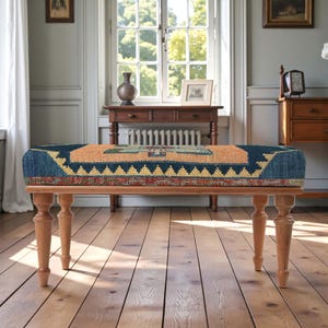 Pu&ograve; includere: Panca in legno con cuscino rettangolare fantasia nei toni del blu, arancione e giallo. La panca ha quattro gambe tornite in legno. Il design del cuscino presenta forme geometriche e un bordo.