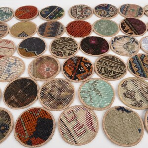 May include: A collection of oval-shaped coasters with intricate rug patterns. The coasters feature a variety of colors, including red, blue, green, and brown, with a beige border. These decorative coasters are ideal for protecting surfaces.