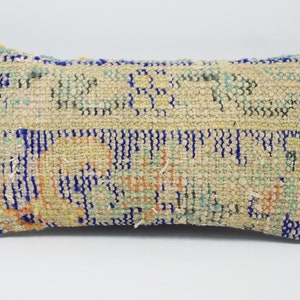 May include: A rectangular throw pillow with a beige background and a colorful geometric pattern in shades of blue, green, orange, and yellow. The pillow is made of woven fabric and has a slightly distressed look.