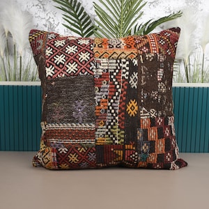 May include: A square cushion with a patchwork design. The cushion features a variety of patterns and colours, including red, brown, orange, and white. The cushion is made of a textured fabric and is likely used for home decor.