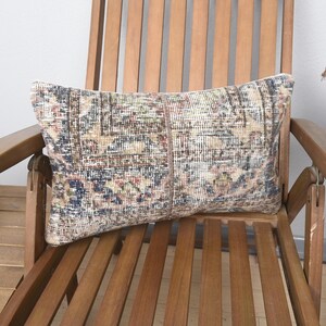 Könnte beinhalten: Ein gemustertes Kissen mit beige-braunem und blauem Design auf einem Holzstuhl.
