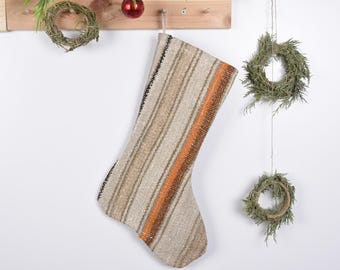 May include: A striped Christmas stocking made from woven fabric with orange, brown, and white stripes. The stocking is hanging from a wooden shelf with a red ornament.