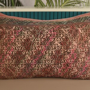 May include: Rectangular decorative pillow with a detailed, patterned design. The pillow features a brown base with pink, green, and white accents. The top edge has a patterned border in shades of green, brown, and pink.