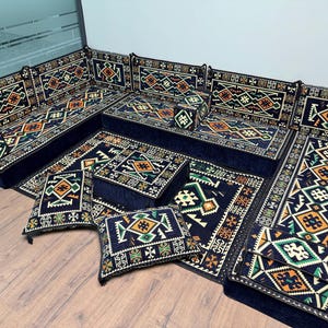 May include: A dark blue modular seating arrangement featuring geometric patterns in orange, green, and white. The set includes cushions and a rug, all with matching designs. The furniture is arranged on a wooden floor, creating a cohesive look.