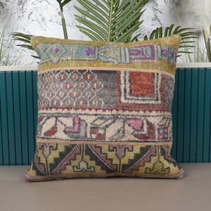 May include: A square decorative pillow with a patchwork design. The pillow features a mix of colors including beige, gray, red, pink, and yellow. The pillow has a textured appearance and is likely made of fabric.