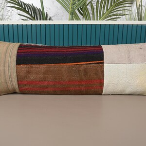 May include: Rectangular decorative pillow with a patchwork design. The pillow features sections of beige, brown, and off-white fabric with striped and solid patterns. The pillow is approximately 12 inches wide and 30 inches long.
