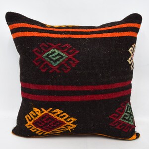 May include: A square throw cushion featuring a dark black base with horizontal orange and deep red stripes. The surface is decorated with embroidered geometric motifs in shades of green, yellow, and red, creating a textured, woven appearance.