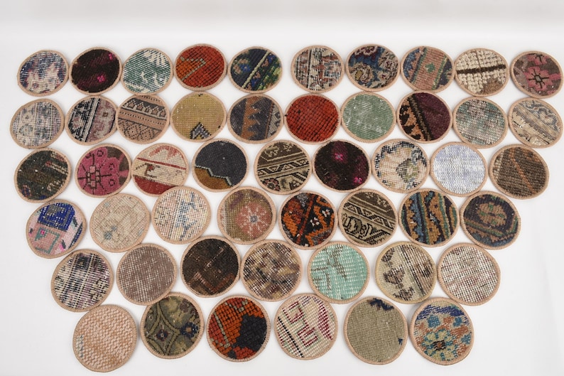 May include: A collection of round coasters with various patterned designs. The coasters feature a variety of colors, including red, blue, green, and brown, with a beige border. The coasters appear to be made from a woven material.