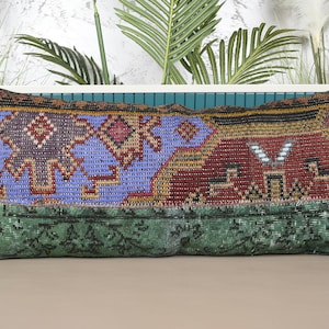 May include: Rectangular decorative pillow with a patchwork design. The pillow features a central section of blue with geometric patterns, flanked by sections of red and green. The edges are dark brown.