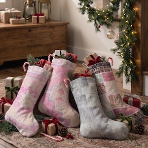 Puede incluir: Cuatro calcetines navideños con patrones de alfombra vintage en tonos rosa, gris y colores tierra. Cada calcetín está relleno con pequeñas cajas de regalo envueltas en papel marrón con lazos rojos y decorado con bastones de caramelo.