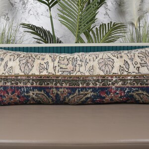 Puede incluir: Cojín decorativo rectangular con diseño de alfombra vintage. El cojín presenta un fondo crema con patrones florales y geométricos en tonos marrón, rojo y azul. El cojín mide aproximadamente 91 cm de largo.