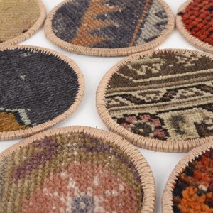 May include: A collection of round coasters with intricate, colorful rug patterns. Each coaster has a beige stitched border. The designs include shades of red, orange, blue, brown, and beige, offering a rustic and decorative touch.