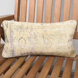 May include: A beige and white patterned throw pillow with a woven texture. The pillow is sitting on a wooden chair.
