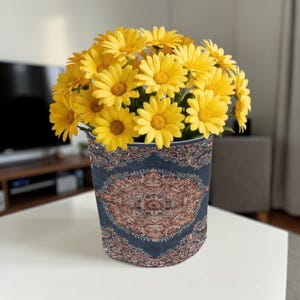 May include: A vase of yellow daisies. The vase has a dark blue background with a detailed, ornate, reddish-brown pattern. The daisies are in full bloom, with yellow petals and brown centres, creating a vibrant floral arrangement.
