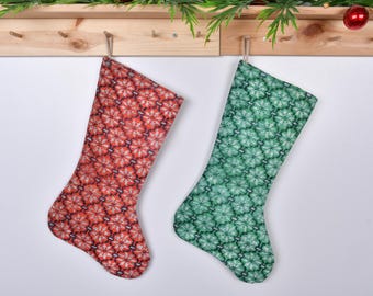 Puede incluir: Dos calcetines de Navidad colgados en un estante de madera. El calcetín de la izquierda es rojo con un patrón de copo de nieve blanco. El calcetín de la derecha es verde con un patrón de copo de nieve blanco.