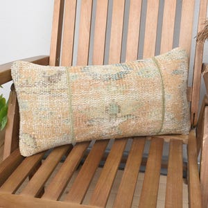 May include: A light brown and beige patterned lumbar pillow with fringe details sits on a wooden chair.
