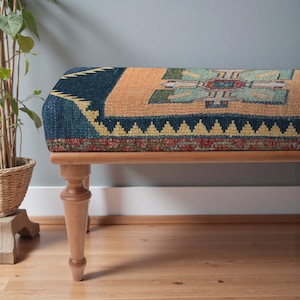May include: Upholstered bench with a patterned top in shades of blue, orange, and green. The bench has a wooden frame and turned legs. The design on the bench top resembles a traditional rug pattern.