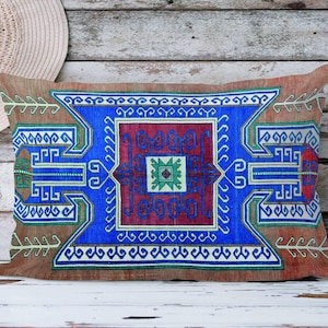 May include: A decorative cushion with a blue, red and green geometric pattern. The cushion has a brown background and a white border.