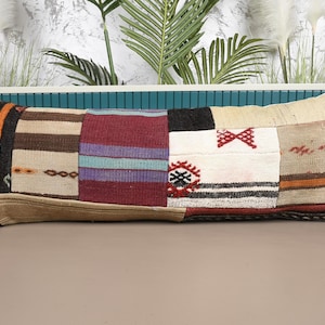 Op de afbeelding: Rechthoekig patchwork kussen met een verscheidenheid aan kleuren en patronen. Het kussen heeft secties van bruine, bordeauxrode, zwarte en witte stof. Sommige secties hebben gestreepte ontwerpen, andere geborduurde details. Het kussen is ongeveer 76 cm lang.