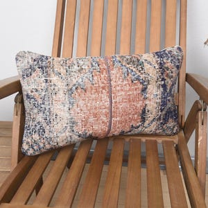 Pode incluir: Um travesseiro de arremesso estampado colorido com um visual desbotado e vintage. O travesseiro está colocado em uma cadeira de madeira com encosto e braços de ripas.