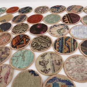May include: A collection of oval-shaped coasters with a woven rug design. The coasters feature various colors and patterns, including red, blue, and beige. Each coaster has a tan border. The coasters are arranged on a white surface.