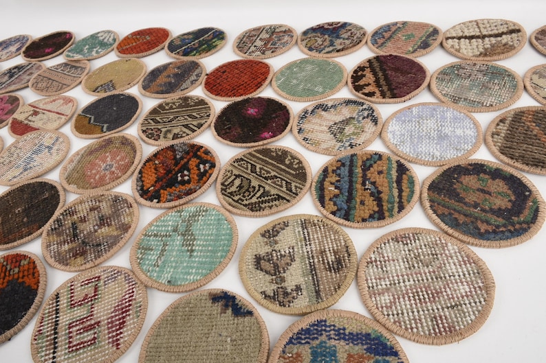 May include: A collection of oval-shaped coasters with a woven rug design. The coasters feature various colors and patterns, including red, blue, and beige. Each coaster has a tan border. The coasters are arranged on a white surface.