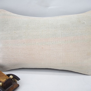 May include: A white pillow with a subtle pink and green striped pattern. The pillow is made of a soft, woven fabric and has a rectangular shape.