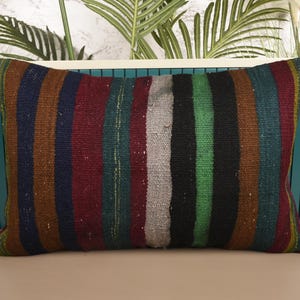 May include: Rectangular pillow with a striped pattern in various colors, including brown, red, green, and black. The pillow is made of a woven fabric and appears to be a decorative item for a home.