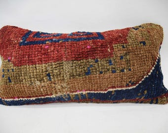 May include: A rectangular pillow with a woven pattern in shades of red, brown, blue, and gold. The pillow has a geometric design with a central square.