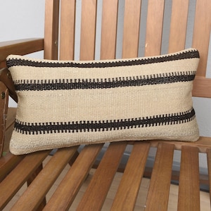 May include: A beige and brown striped throw pillow with a woven texture. The pillow is sitting on a wooden chair.