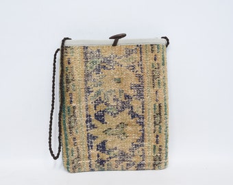 May include: A small, beige and blue patterned bag with a brown strap. The bag is made from a woven fabric and has a simple design.