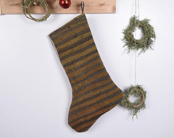 May include: A striped Christmas stocking with a brown and gold color scheme. The stocking is hanging from a hook on a wooden surface.