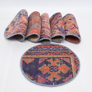 May include: Set of six round, colorful, patterned coasters with a blue trim. The coasters are made of fabric and have a traditional design.