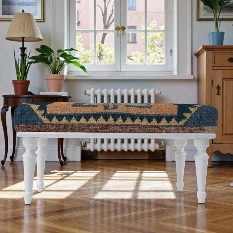 Pu&ograve; includere: Una panca bianca con una seduta rettangolare con un motivo nei toni del blu, beige e rosso. La panca ha quattro gambe tornite bianche ed &egrave; posta davanti a una finestra. La stanza ha un pavimento in parquet. La panca &egrave; lunga circa 120 cm.