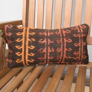 May include: A brown and orange patterned throw pillow with a geometric design. The pillow is sitting on a wooden chair.