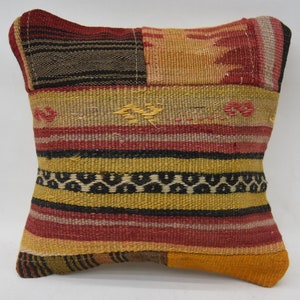 May include: A square decorative pillow with a patchwork design. The pillow features a mix of colors including red, yellow, black, and brown. The fabric has a woven texture with horizontal stripes and geometric patterns. The pillow is likely used for home decor.