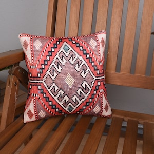 May include: A red, white, and blue patterned throw pillow with a geometric design. The pillow is sitting on a wooden chair.