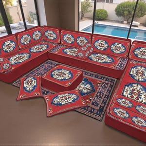 Puede incluir: Un sofá esquinero rojo con cojines estampados y una alfombra a juego. Los cojines y la alfombra presentan un diseño de medallón central en azul, blanco y beige sobre un fondo azul oscuro. El sofá está dispuesto en forma de L.