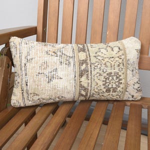 May include: A beige and brown patterned throw pillow with a woven texture sits on a wooden chair.