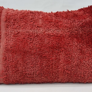 May include: Red throw pillow with a fuzzy, textured surface. The pillow is rectangular and has a slightly frayed edge.