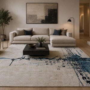 Peut inclure: Un tapis rectangulaire au fond beige clair orné de motifs abstraits en forme d'éclaboussures d'encre bleu foncé et noir, avec des lignes marquées concentrées sur le côté droit, recouvrant le sol d'un salon.