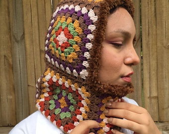 May include: A brown crocheted hooded scarf with a faux fur lining. The scarf is made with colorful granny squares in shades of brown, orange, green, purple, and white.