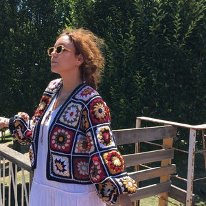 May include: A colorful crocheted jacket with a black background and a variety of colored squares. The jacket has a V-neck and long sleeves.